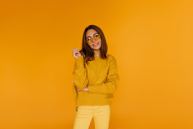 Garota atraente em calças amarelas sorrindo. Lindo modelo feminino caucasiano de óculos, desfrutando da sessão de fotos.