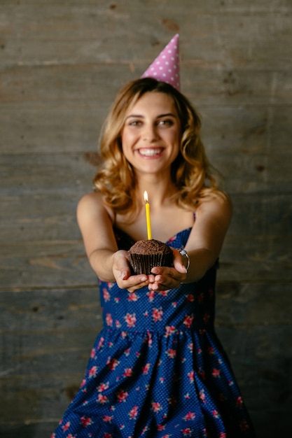 Garota atraente feliz detém um bolo de chocolate com vela, comemorando seu aniversário