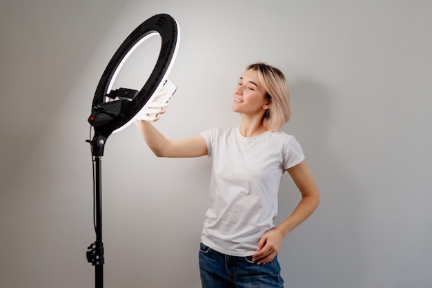 Garota blogueira está transmitindo ao vivo por meio de um smartphone sob uma lâmpada circular