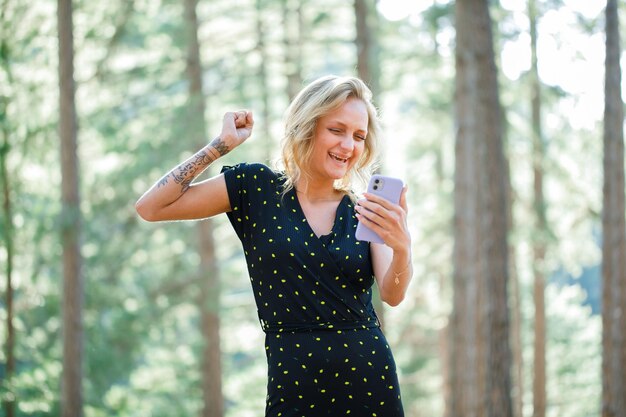 Garota blogueira feliz está levantando o punho falando em videochamada no fundo da natureza