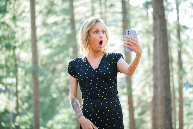 Garota blogueira surpresa está tomando sefie com seu celular no fundo da natureza