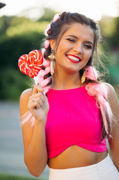 Garota bonita e positiva no top rosa segurando o coração de doces na vara.