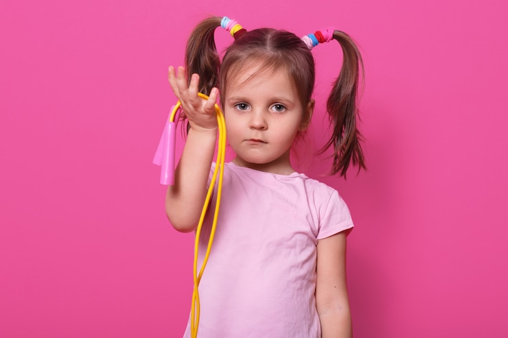Foto grátis garota bonita e triste segura na mão pulando corda. criança quer brincar com alguém. criança adorável com caudas de pônei e scrunchies coloridos, veste camiseta na rosa.