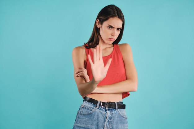 Garota casual com raiva olhando tristemente na câmera mostrando gesto de parada sobre fundo colorido isolado