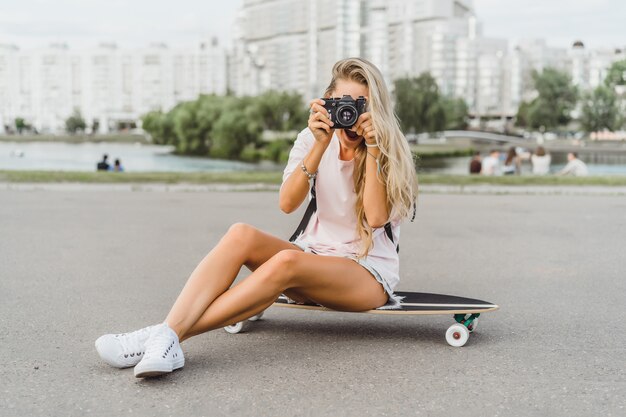 garota com cabelo comprido com skate fotografando na câmera. rua, esportes ativos