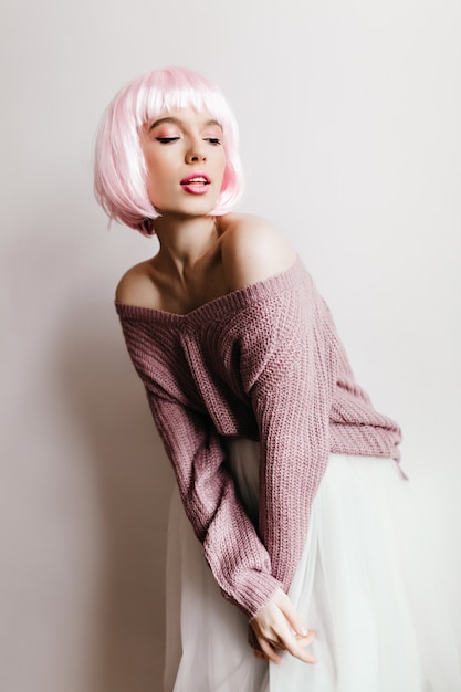 garota com cabelo rosa claro, posando com saia branca. Foto interna de uma jovem europeia pensativa usa peruca curta.