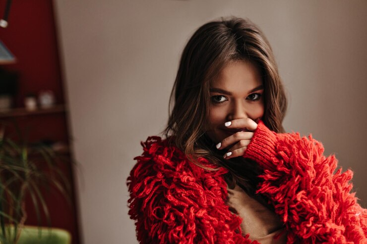 Foto grátis garota com manicure branca cobre a boca com a mão e olha para a câmera coquetemente instantâneo da morena na jaqueta de malha vermelha