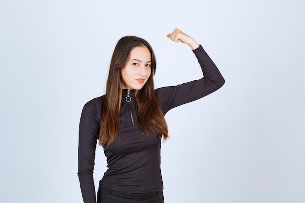 Garota com roupas pretas, mostrando os músculos do punho e do braço.