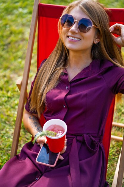 garota com um smartphone e um coquetel na natureza em uma espreguiçadeira. Dia de verão de folga.