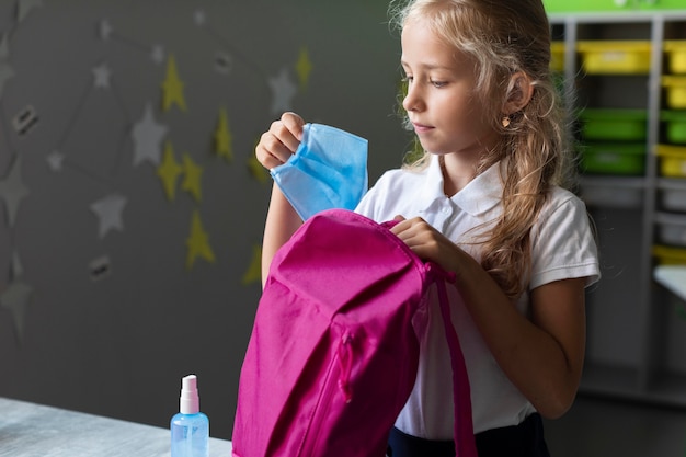 Foto grátis garota com vista lateral colocando sua máscara médica em uma mochila