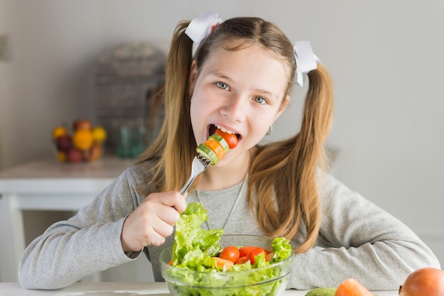 Garota comendo salada de legumes com garfo