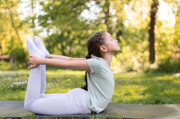 Garota completa se exercitando em um tapete de ioga do lado de fora
