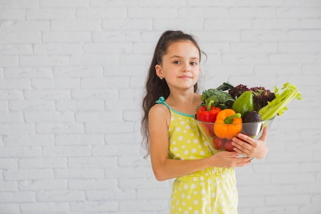 Garota confiante em frente a parede segurando a tigela de legumes