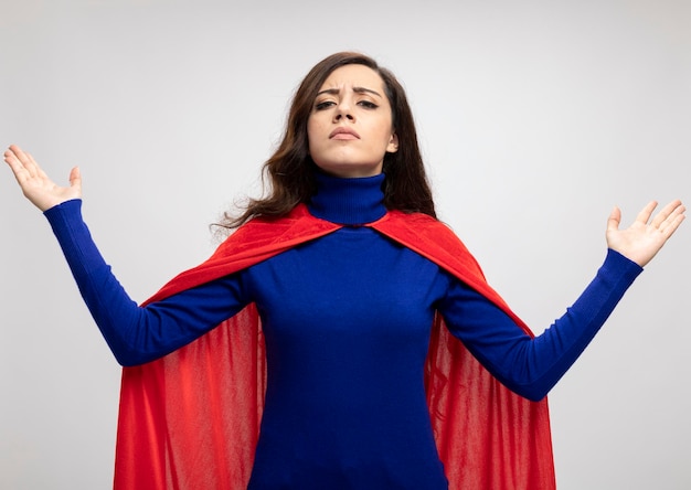 Foto grátis garota confiante super-heroína caucasiana com capa vermelha fica com as mãos levantadas em branco