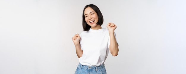 Garota coreana dançando feliz posando contra um fundo branco vestindo camiseta