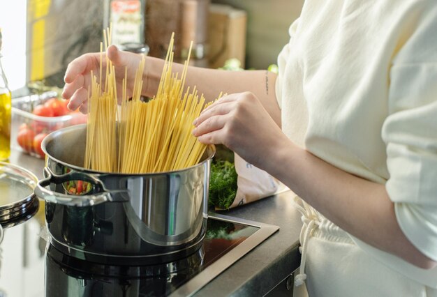 Garota cozinhando macarrão espaguete na panela