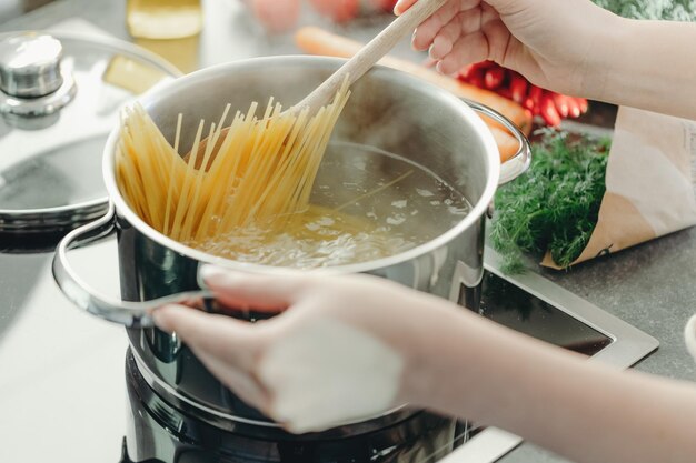 Garota cozinhando macarrão espaguete na panela