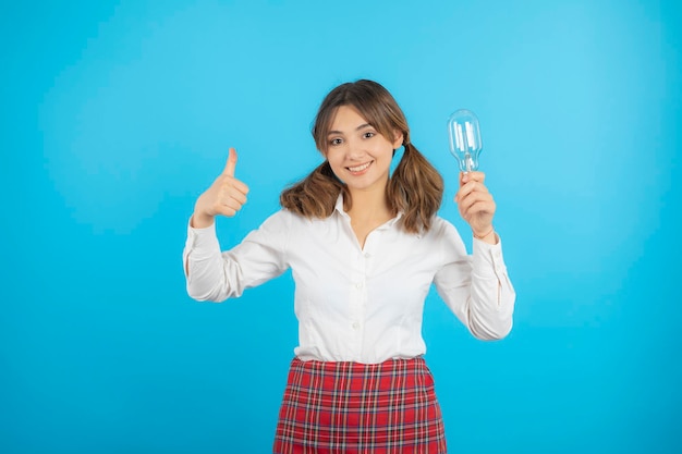 Garota da faculdade jovem segurando a luz e gesticulando o polegar para cima. Foto de alta qualidade