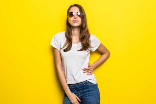 Garota da moda jovem em camiseta branca e jeans azul fica na frente do fundo amarelo do estúdio