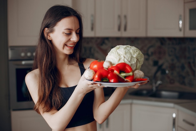 Garota de esportes em uma cozinha com legumes