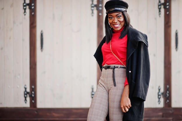 Garota de moda afro-americana de casaco e boné de jornaleiro posou na rua