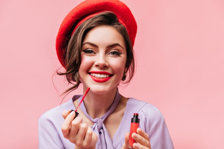 Foto grátis garota de olhos verdes com sorriso branco como a neve pinta os lábios com batom vermelho. retrato de senhora de boina elegante em fundo rosa.
