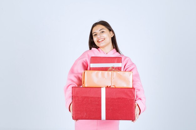 Garota de pijama rosa segurando várias caixas de presente vermelhas e se sentindo feliz.