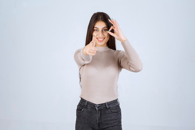Garota de suéter cinza mostrando sinal de ok do círculo.