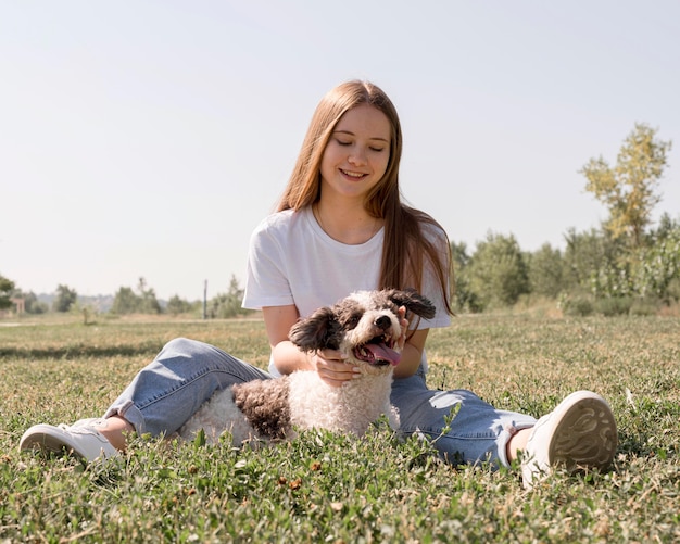 Garota de tiro completo sentada na grama com um cachorro