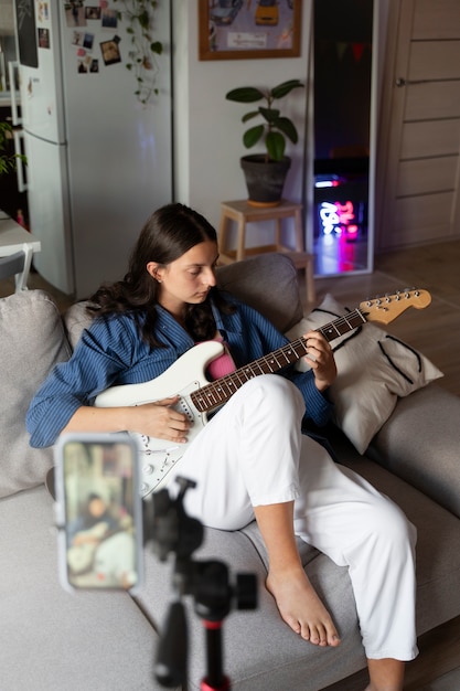 Garota de tiro completo tocando guitarra dentro de casa