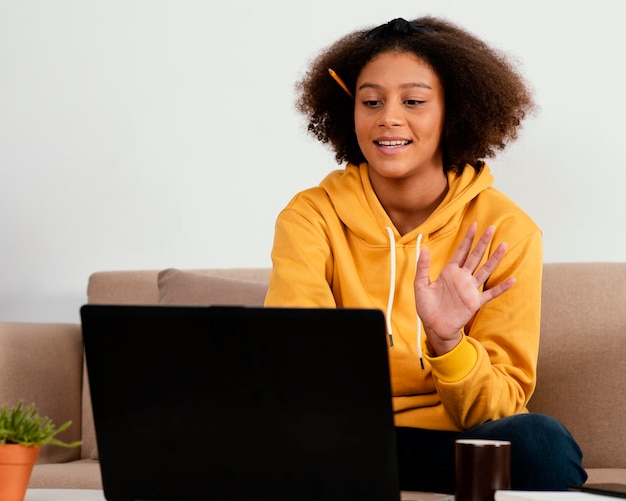 Garota de tiro médio acenando para um laptop