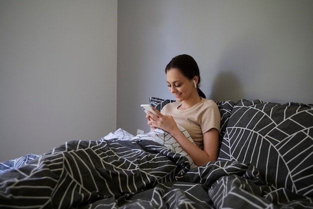 Garota de tiro médio na cama com smartphone