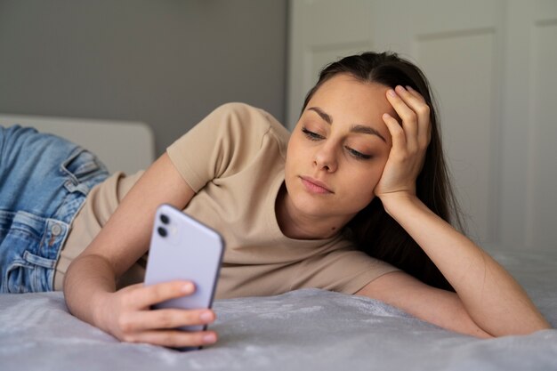 Garota de tiro médio na cama com smartphone