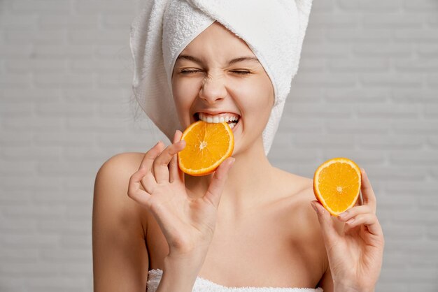 Garota de toalha segurando dois pedaços de laranja e mordendo
