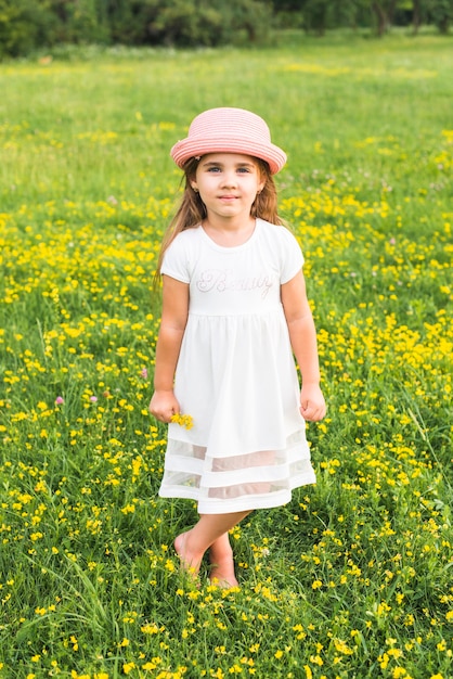 Garota de vestido branco em pé no Prado segurando flores amarelas