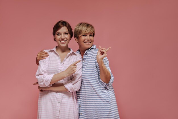 Garota de vestido rosa listrado sorrindo mostrando lugar para texto e abraçando com uma velha loira com roupa azul em pano de fundo isolado