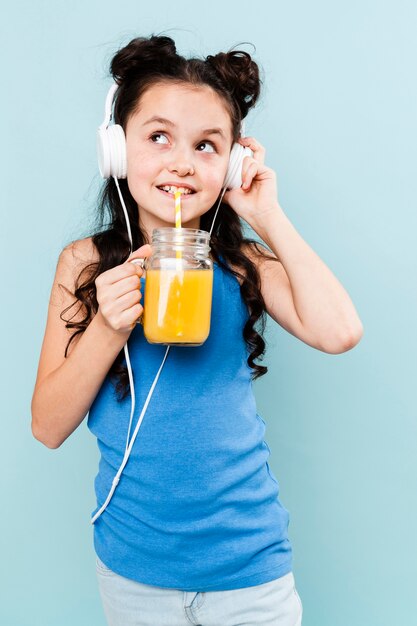 Garota de vista frontal bebendo suco e ouvindo música