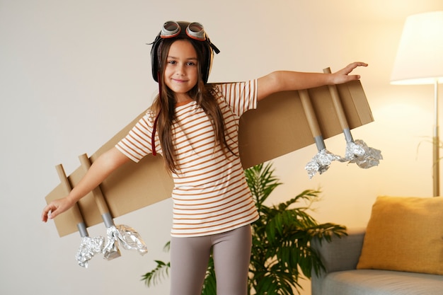 Foto grátis garota de vista frontal brincando com asas de papelão