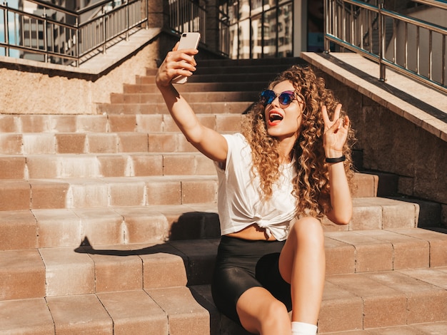 Garota despreocupada, sentado na escada na rua tomando uma selfie