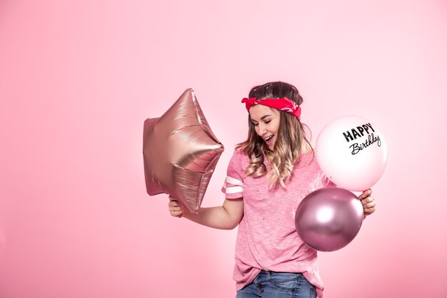 Garota divertida em uma camiseta rosa com balões Feliz aniversário sorri e emociona