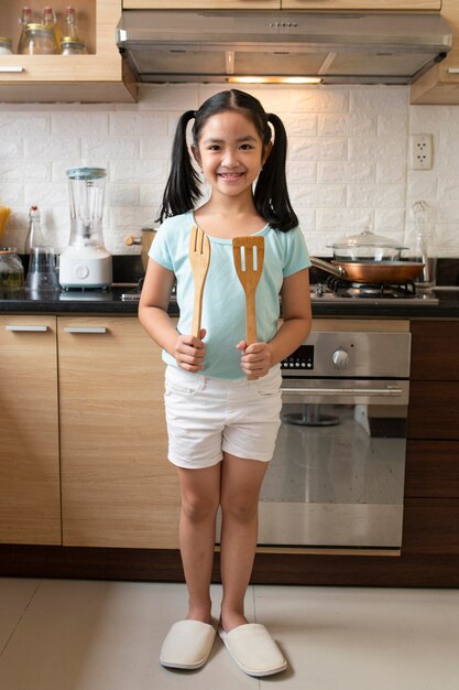 Garota em cena completa segurando utensílios de cozinha