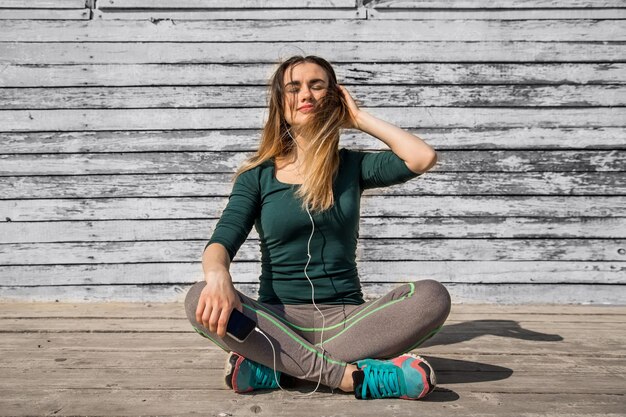 Garota em roupas esportivas, ouvindo música, motivação esportiva, esportes, fitness, garota fitness sentada no fundo de madeira