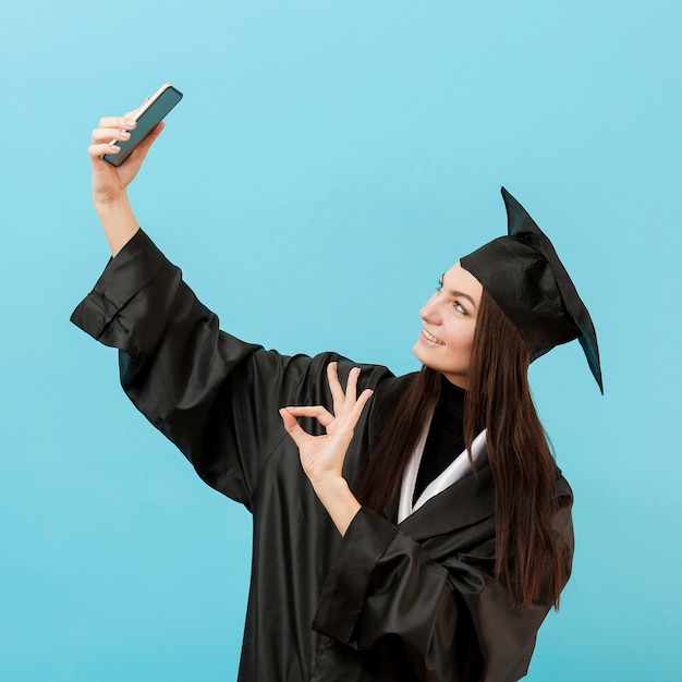 Garota em traje acadêmico tomando selfie