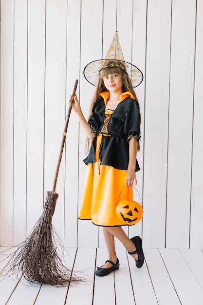 Garota em traje de halloween com vassoura posando no estúdio
