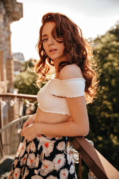 Garota encantadora com roupa moderna floral olha para a câmera Foto de uma jovem brilhante em roupas elegantes de verão posando bonitinho
