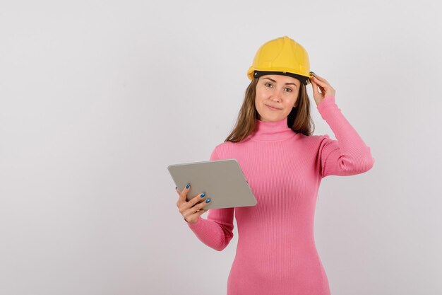 Garota engenheira com computador tablet está segurando seu capacete no fundo branco