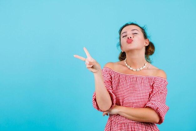 Garota engraçada está mostrando mímica de beijo e dois gestos em fundo azul