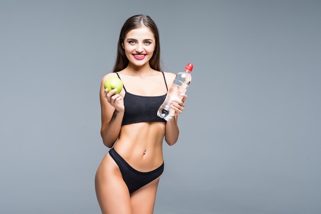 Garota esportiva na cueca segurando a garrafa de água com maçã verde e mostrando os músculos isolados no branco