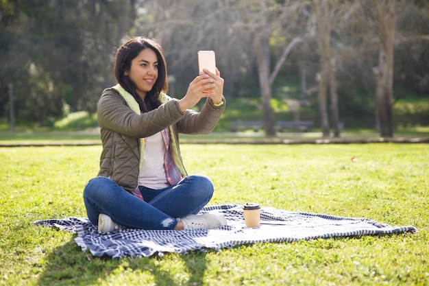 Garota estudante animada descansando no parque e tomando selfies