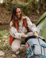 Foto grátis garota feliz acampando na floresta olhando para a mochila
